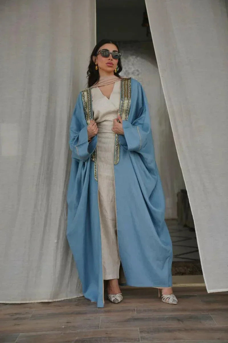 woman wearing soft blue linen bisht with golden embroidery and wide sleeves standing indoors