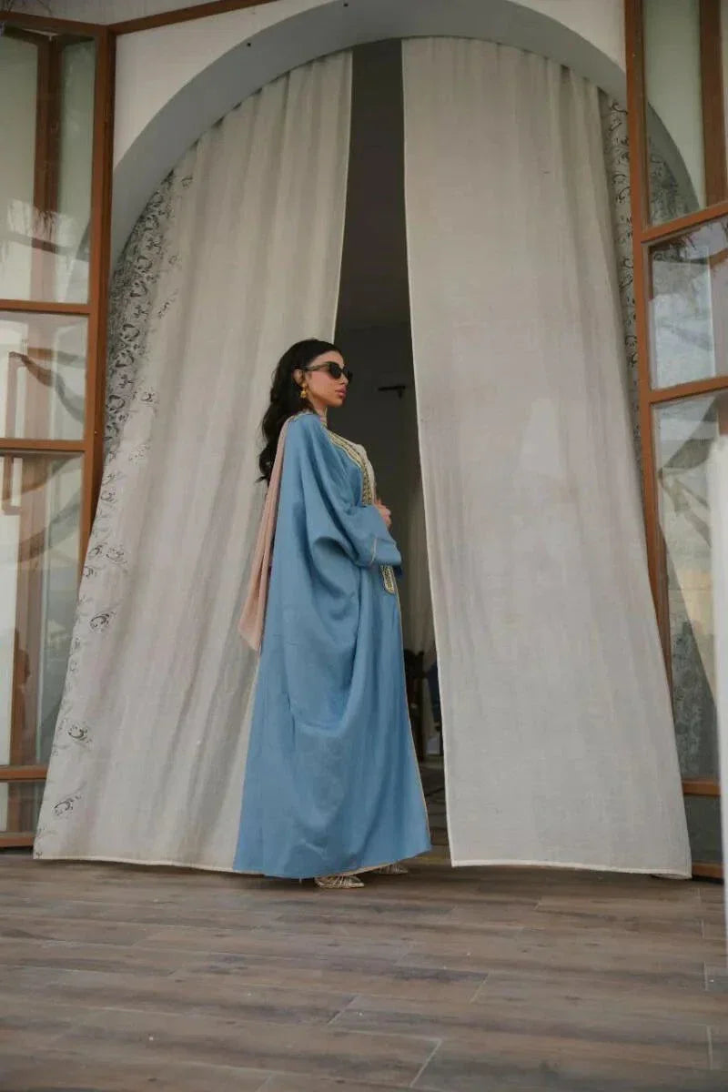 woman wearing soft blue linen bisht with golden embroidery and wide sleeves standing indoors