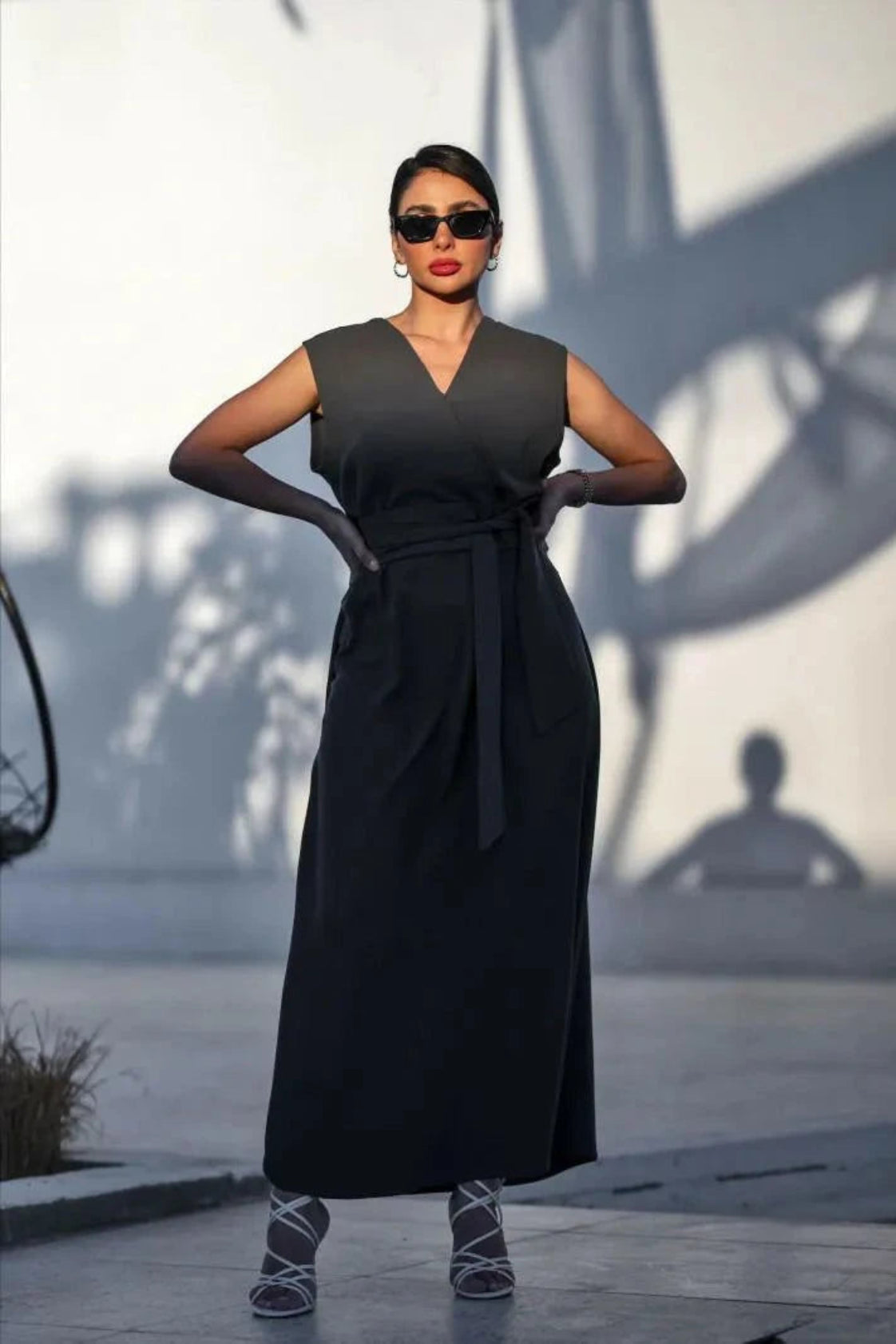 Woman wearing sleeveless dark gray crepe dress with V-neckline and waist tie outdoors