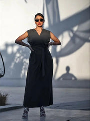 Woman wearing sleeveless dark gray crepe dress with V-neckline and waist tie outdoors