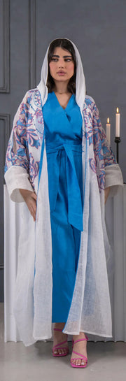 White bisht made of airy linen with bold blue and soft pink floral embroidery, loose fit, hooded design, worn over a blue dress.