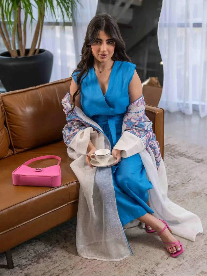 white bisht with blue and pink floral embroidery, lightweight linen fabric, loose fit with hood, styled over blue dress