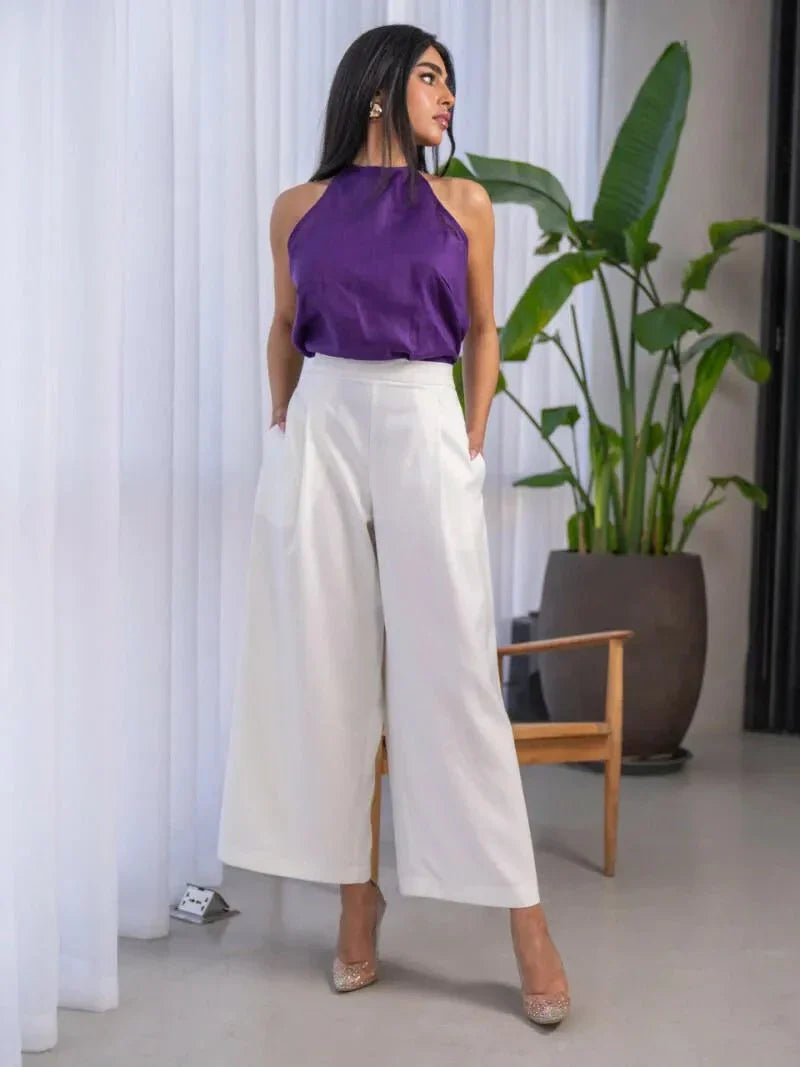 Woman wearing a white and purple set with a sleeveless halter-neck purple top and high-waisted white wide-leg pants with side pockets.