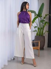 Woman wearing a white and purple set with a sleeveless halter-neck purple top and high-waisted white wide-leg pants with side pockets.