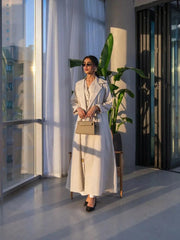 Woman wearing a beige linen blazer-style abaya with classic lapel collar and front buttons in a modern, sunlit room