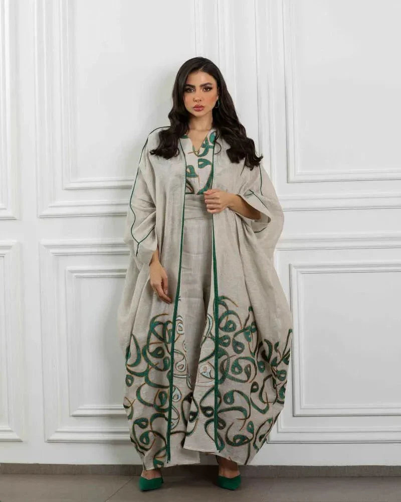 Woman wearing beige linen three-piece set with sleeveless dress, wide-leg pants, and flowing outer layer featuring green calligraphy-inspired embroidery and deep green trim