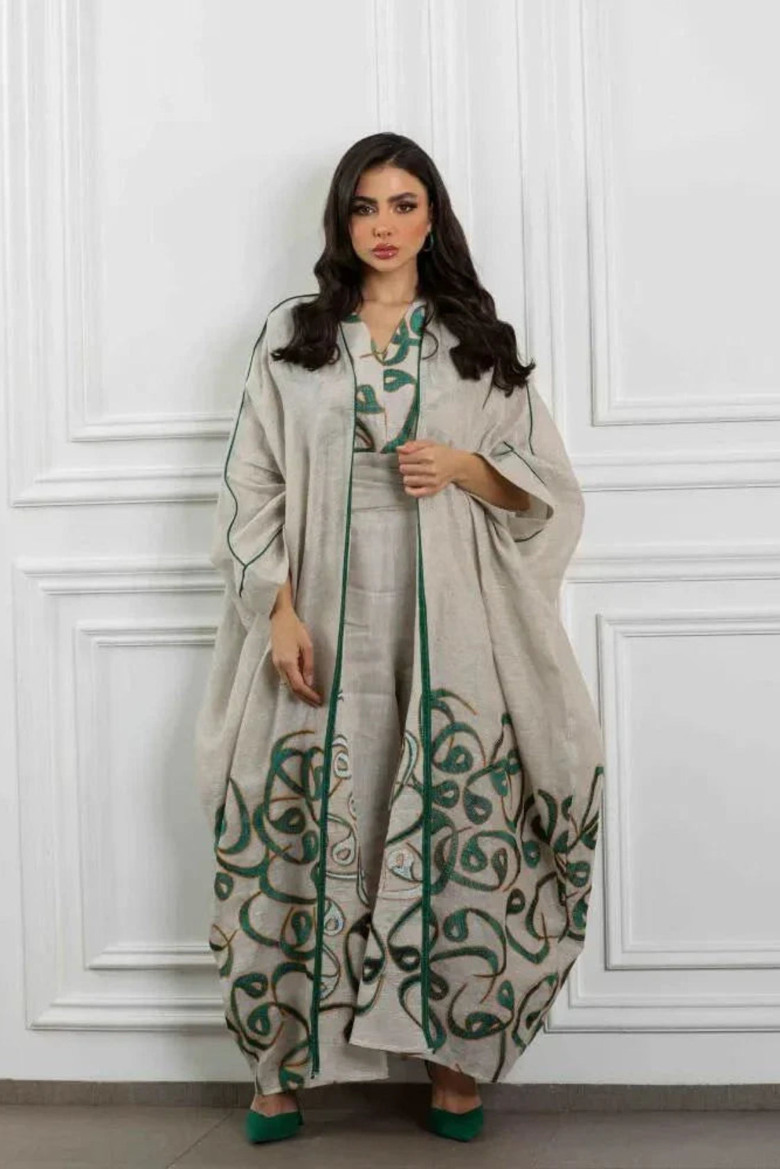 Woman wearing beige linen three-piece set with sleeveless dress, wide-leg pants, and flowing outer layer featuring green calligraphy-inspired embroidery and deep green trim