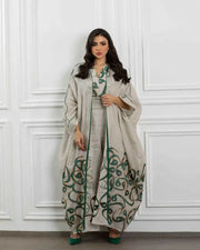 Woman wearing beige linen three-piece set with sleeveless dress, wide-leg pants, and flowing outer layer featuring green calligraphy-inspired embroidery and deep green trim