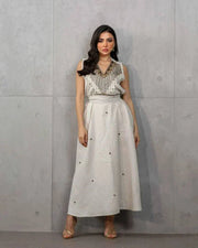 Woman wearing a beige three-piece linen set with sleeveless embroidered top, high-waisted skirt, and matching shawl with stitched accents.