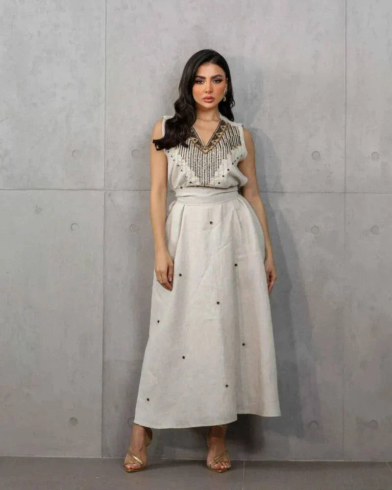 Woman wearing a beige three-piece linen set with sleeveless embroidered top, high-waisted skirt, and matching shawl with stitched accents.
