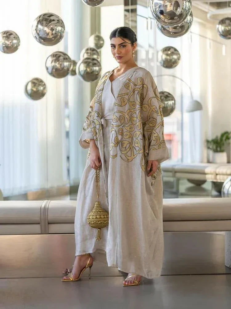 beige linen bisht with gold embroidery and wide sleeves worn by woman in modern indoor setting