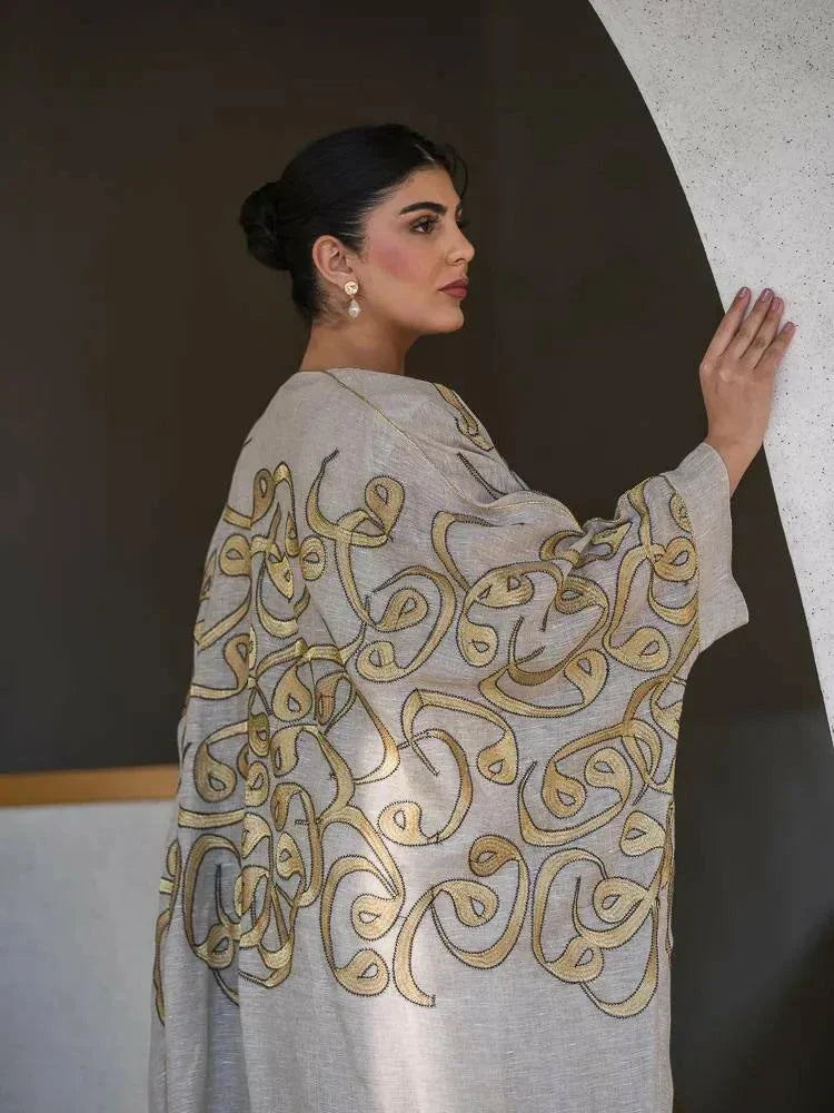 beige linen bisht with gold embroidery and wide sleeves worn by woman in modern indoor setting