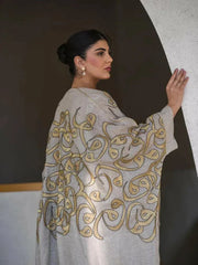 beige linen bisht with gold embroidery and wide sleeves worn by woman in modern indoor setting