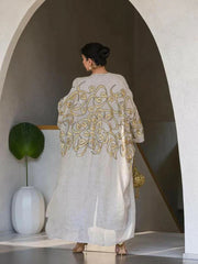 beige linen bisht with gold embroidery and wide sleeves worn by woman in modern indoor setting
