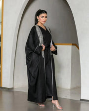 Woman wearing luxurious black linen bisht with silver embellished neckline and sleeve piping in elegant draped silhouette