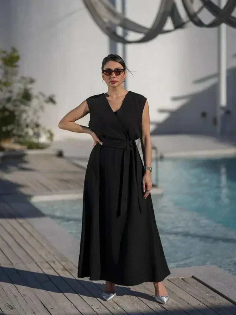 woman wearing sleeveless black wrap dress with waist tie standing by poolside