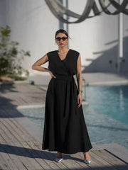 woman wearing sleeveless black wrap dress with waist tie standing by poolside