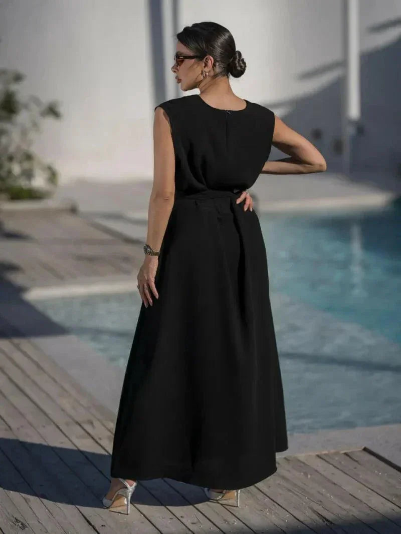 woman wearing sleeveless black wrap dress with waist tie standing by poolside