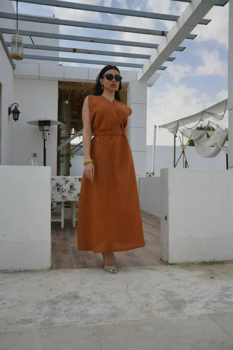 Woman wearing a sleeveless rust-toned linen dress with a V-neckline and waist belt standing outdoors under a pergola - Rustina
