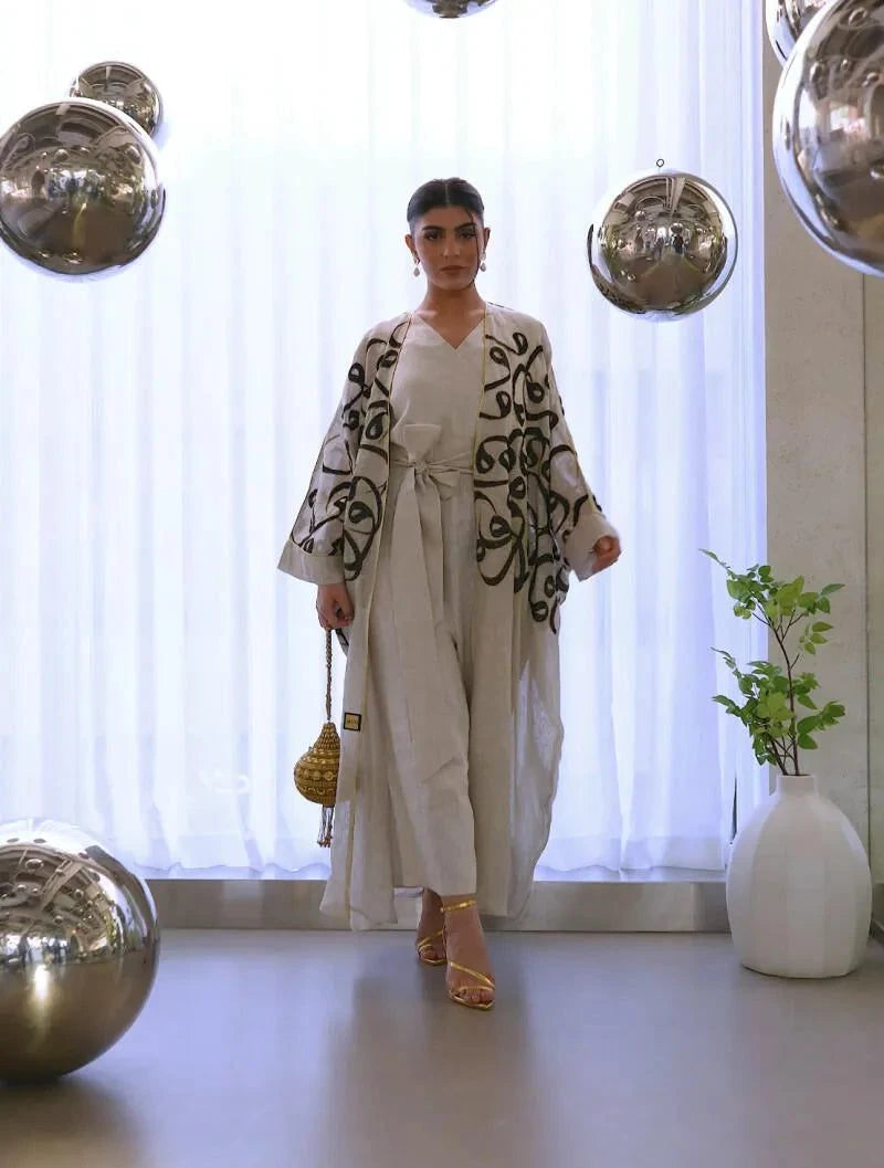 woman wearing natural beige statement linen bisht with bold black calligraphy embroidery in modern elegant setting