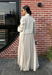 Woman wearing Whisper Beige linen abaya with pleated chiffon panels and double-breasted buttons, styled with a white top, beige skirt, and heels.
