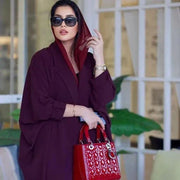 Woman wearing a stylish burgundy blazer abaya made from premium crepe fabric, accessorized with sunglasses and a red handbag.