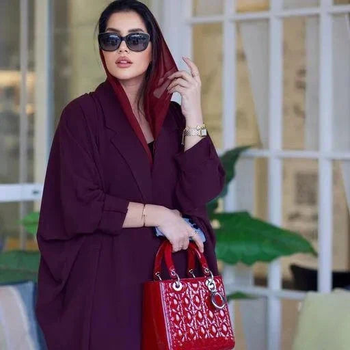 Woman wearing a stylish burgundy blazer abaya made from premium crepe fabric, accessorized with sunglasses and a red handbag.