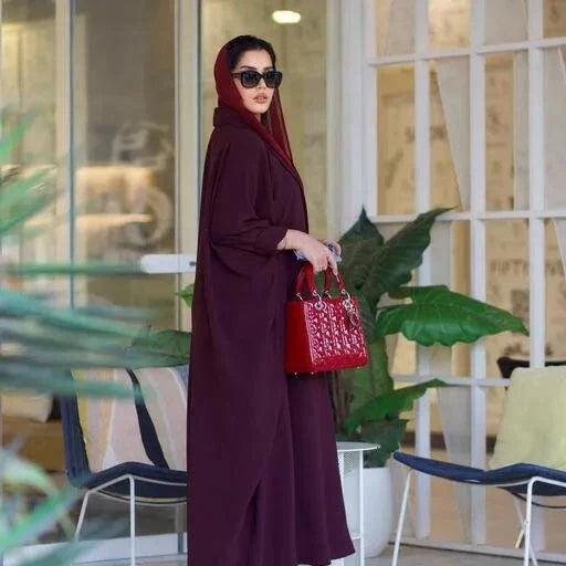 Woman wearing a stylish burgundy blazer abaya made from premium crepe fabric, accessorized with sunglasses and a red handbag.
