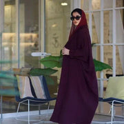 Woman wearing a stylish burgundy blazer abaya made from premium crepe fabric, accessorized with sunglasses and a red handbag.