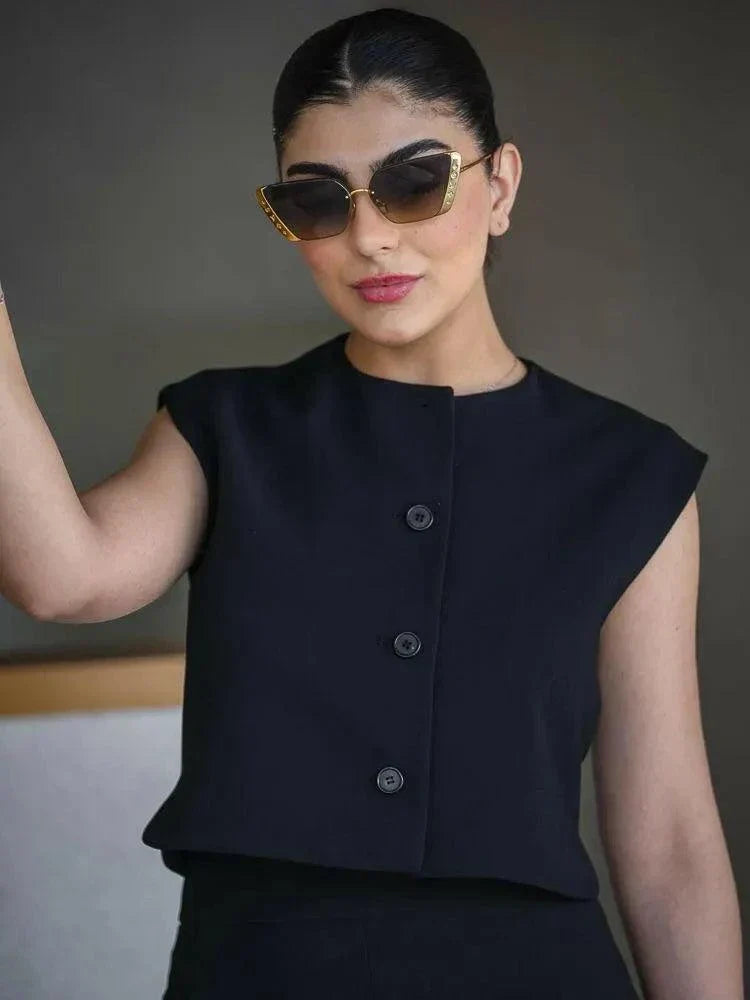 Woman wearing a sleek sleeveless black crepe vest with a round neckline and three front buttons, styled with sunglasses.