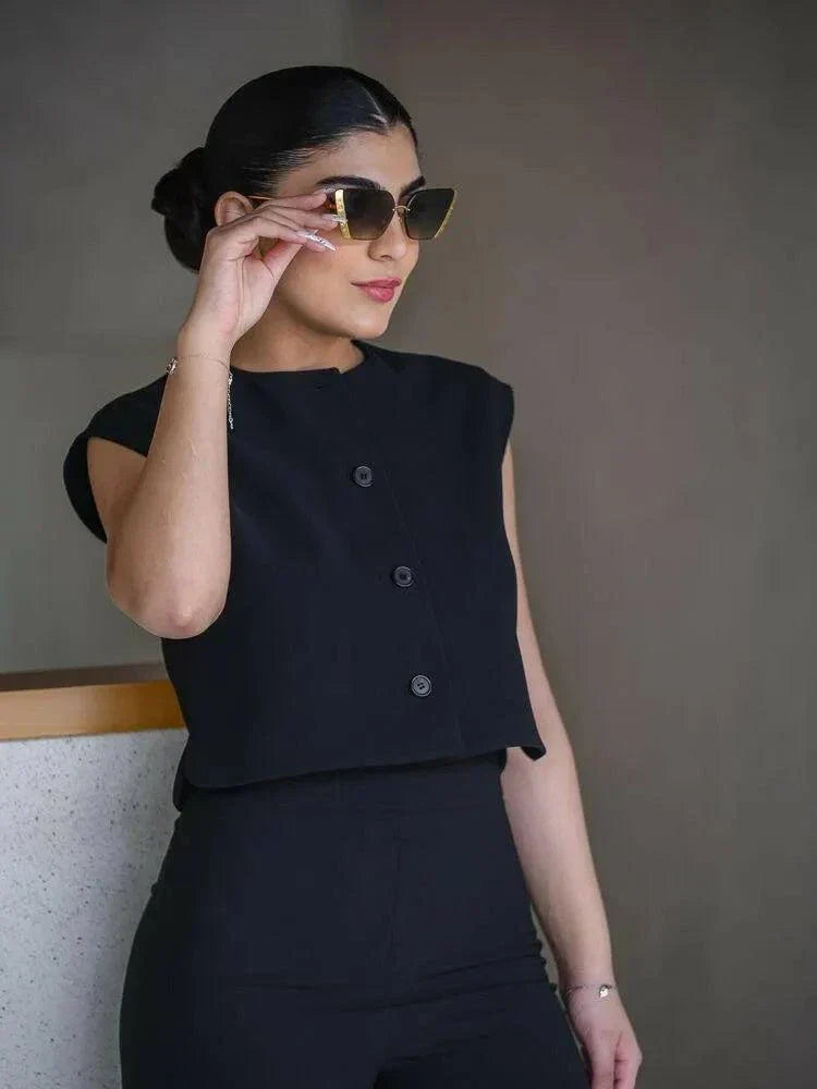  Woman wearing a sleek sleeveless black crepe vest with a round neckline and three front buttons, styled with sunglasses.
