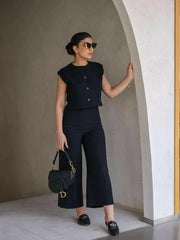  Woman wearing a sleek sleeveless black crepe vest with a round neckline and three front buttons, styled with sunglasses.