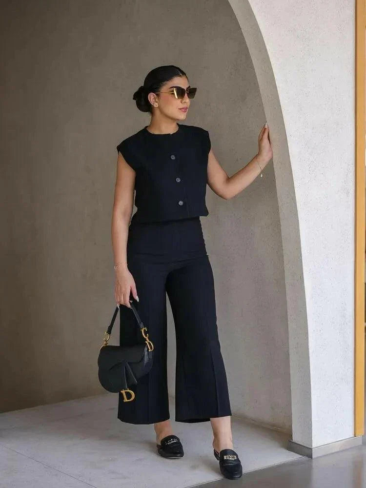 Woman wearing a sleek sleeveless black crepe vest with a round neckline and three front buttons, styled with sunglasses.