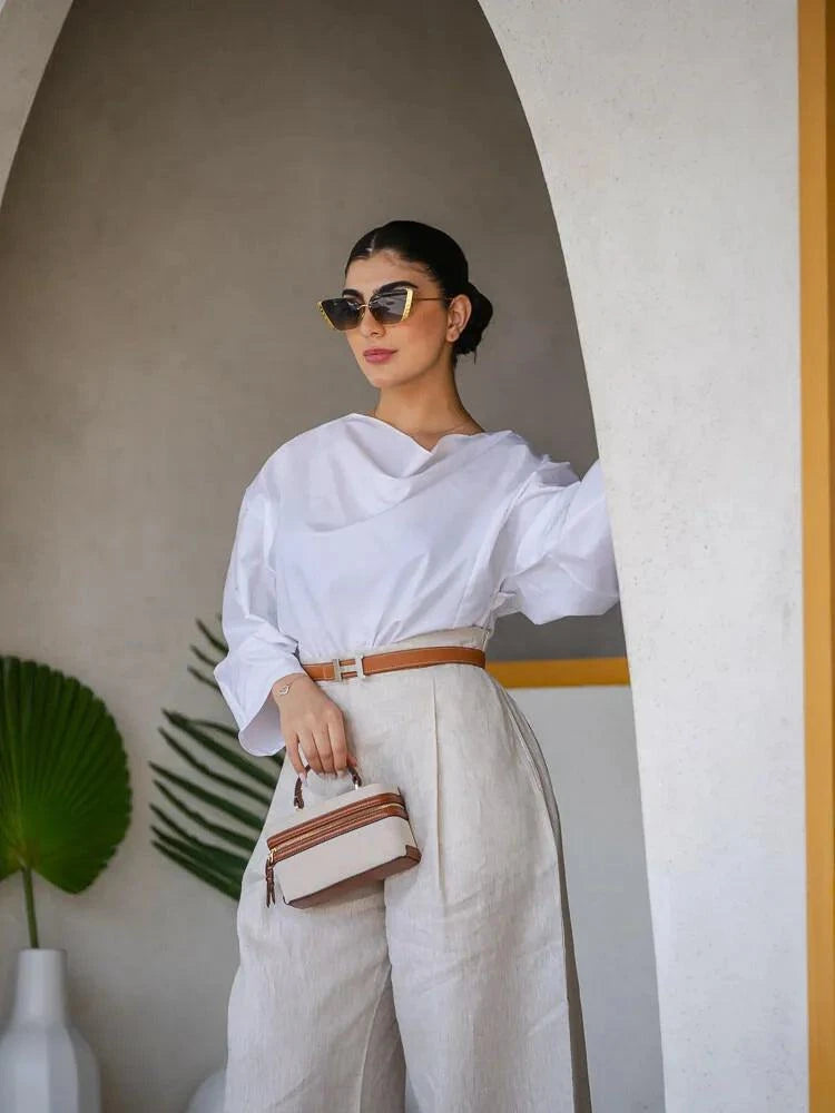 woman wearing cotton white blouse with draped neckline and wide sleeves paired with beige pants and sunglasses