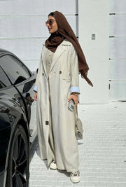 light beige linen blazer-style abaya with double-breasted front, structured shoulders, notched lapels, and contrast striped inner cuffs for sophisticated daily wear