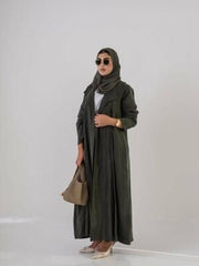 Woman wearing a lightweight olive green Cobra silk abaya with a soft cloche cut and back pleats, styled with a matching headscarf, sunglasses, beige handbag, and beige heels.