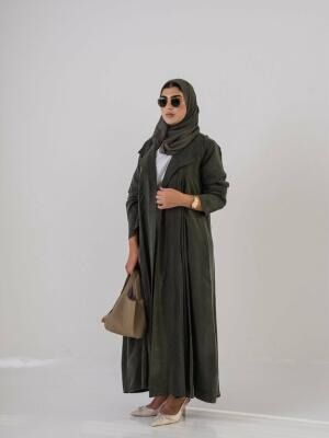 Woman wearing a lightweight olive green Cobra silk abaya with a soft cloche cut and back pleats, styled with a matching headscarf, sunglasses, beige handbag, and beige heels.