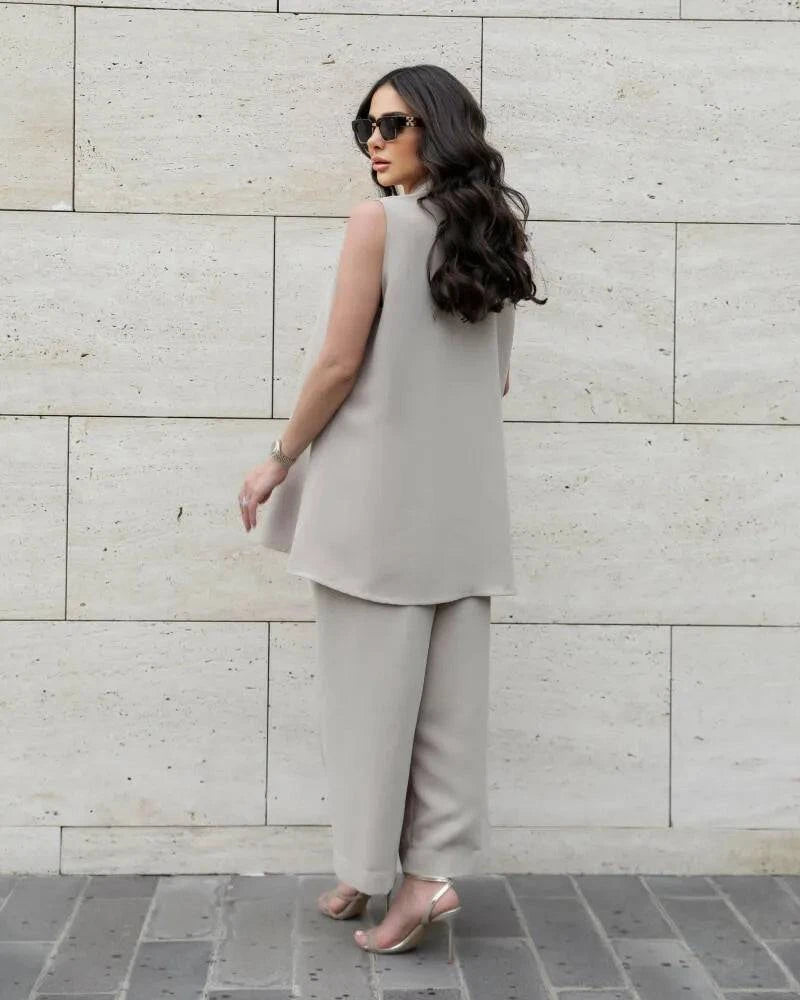 Woman wearing a stylish light beige sleeveless double-breasted vest and wide-leg pants inner set with sunglasses and handbag against a stone wall background