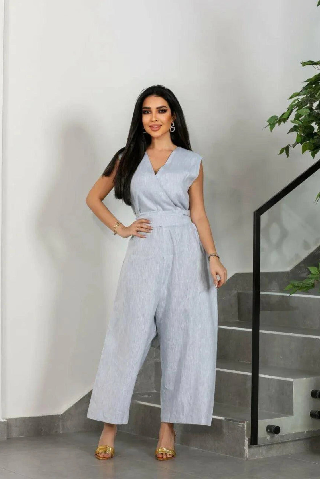 Woman wearing gray linen sleeveless jumpsuit with wide waist tie and wide-leg cut standing indoors