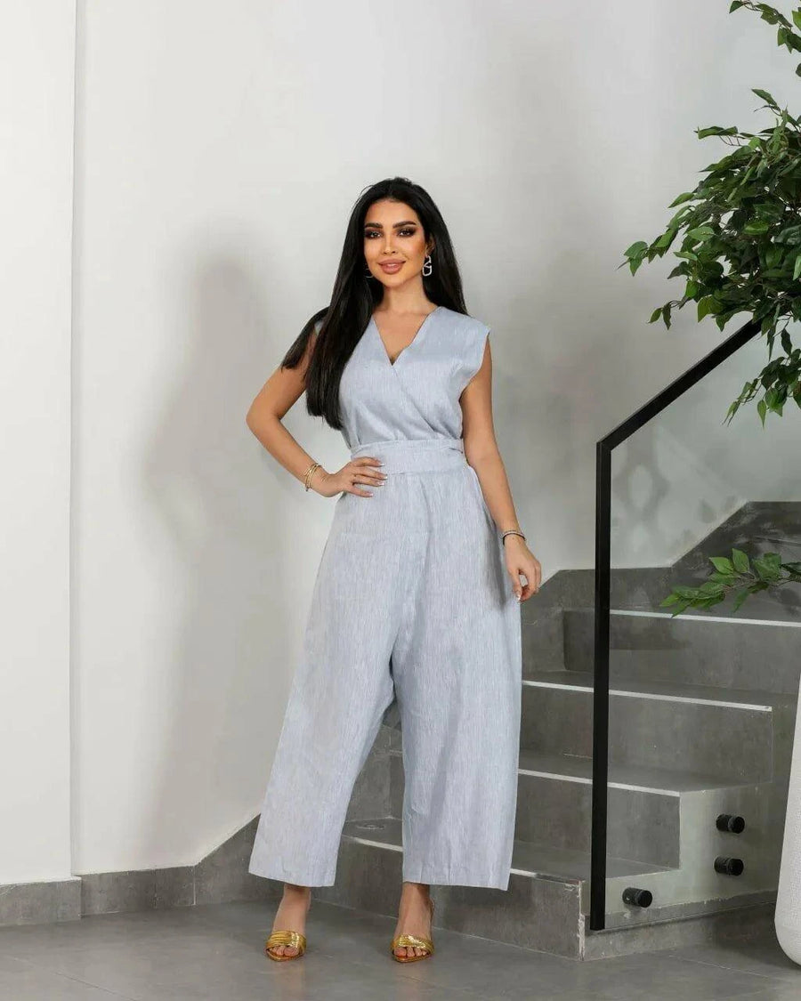 Woman wearing gray linen sleeveless jumpsuit with wide waist tie and wide-leg cut standing indoors