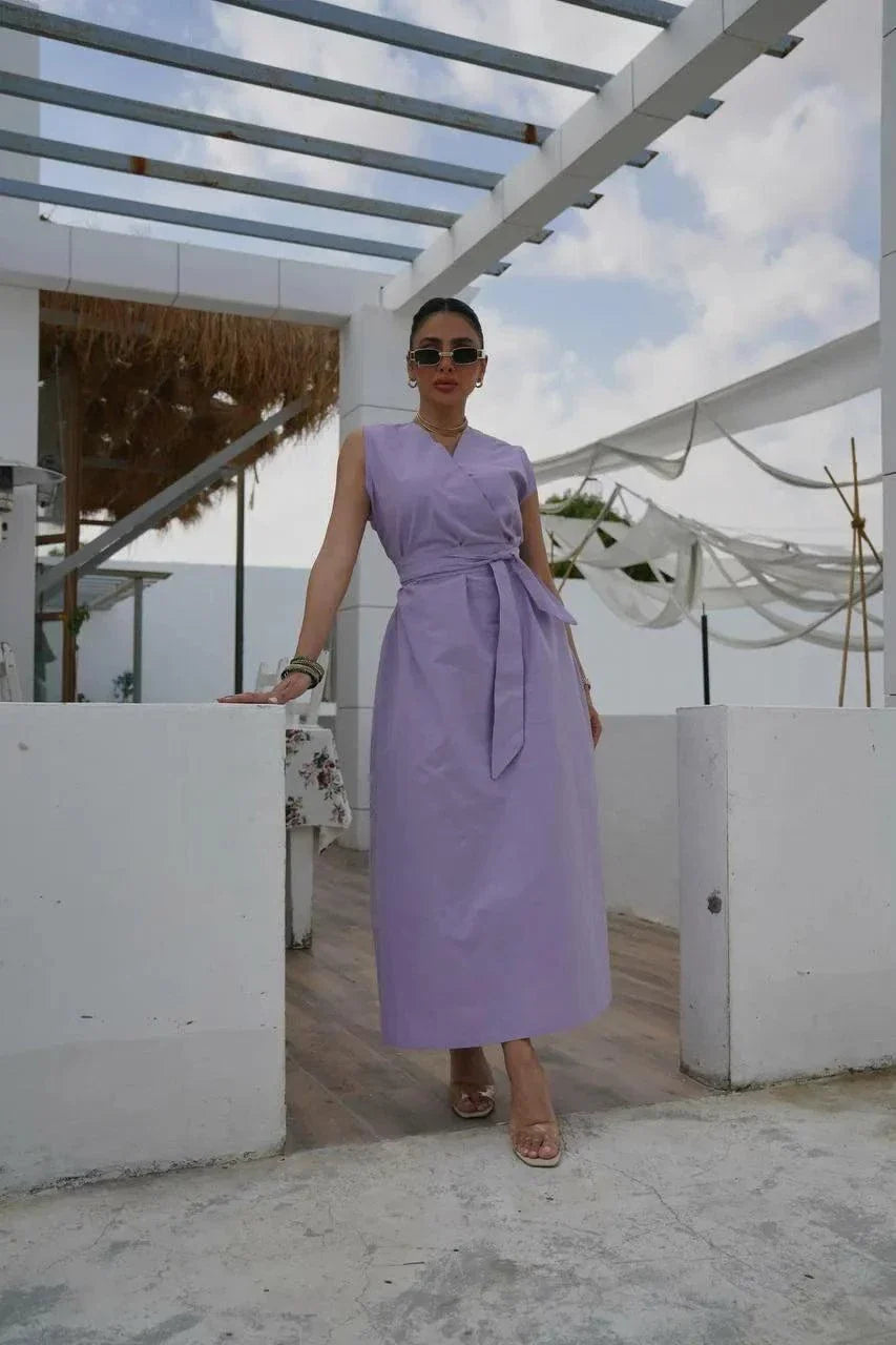 Woman wearing a soft purple orchid linen dress with a relaxed silhouette and tied waist, standing outdoors under a pergola.