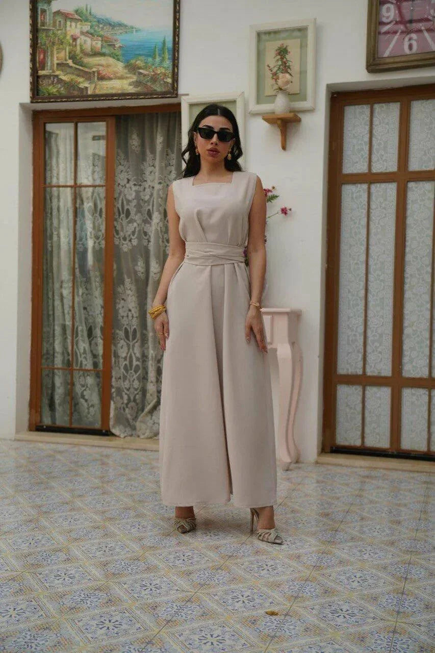 Woman wearing sleeveless latte jumpsuit with square neckline and wide waist tie in a stylish indoor setting