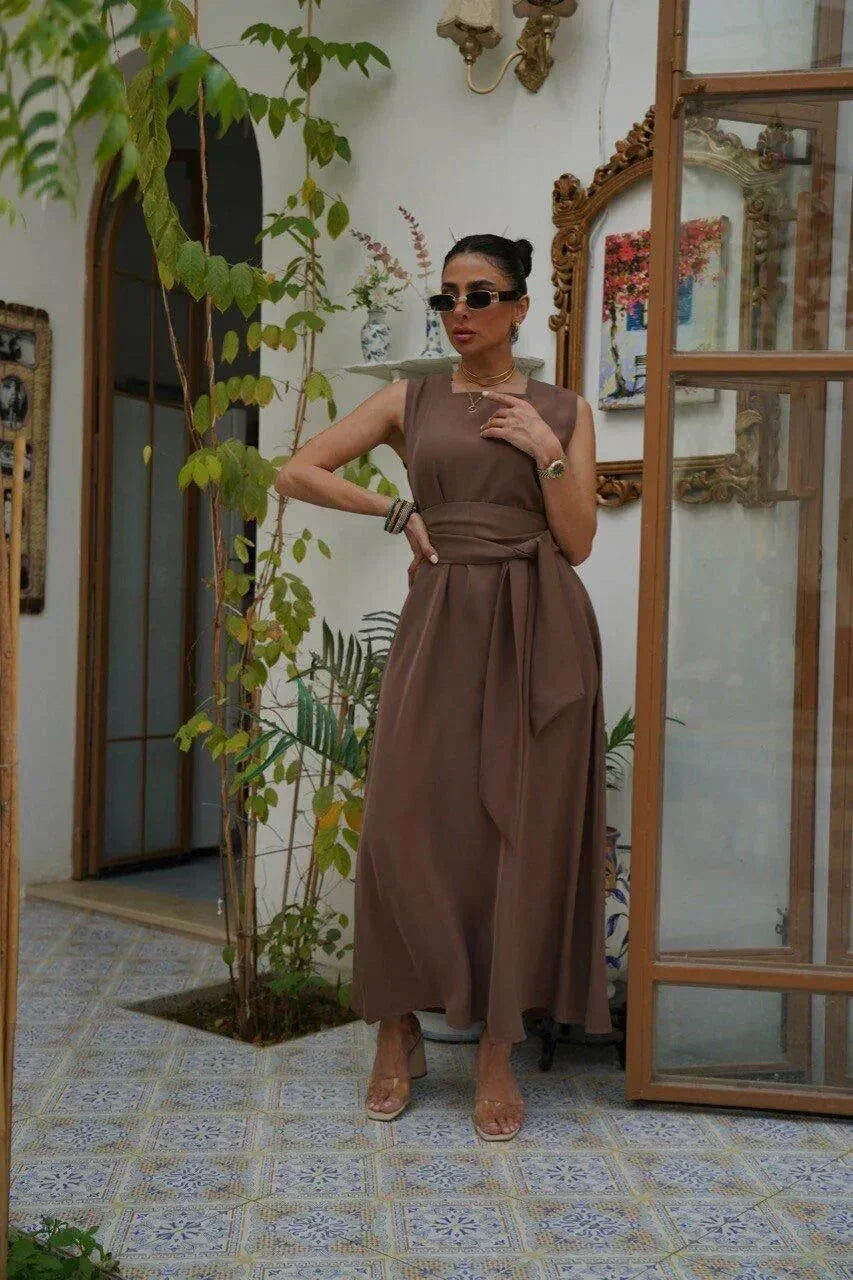 Woman wearing a sleeveless brown crepe dress with a wide waist tie, standing indoors by an open door - sleeveless dress