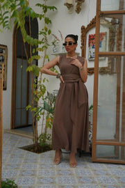 Woman wearing a sleeveless brown crepe dress with a wide waist tie, standing indoors by an open door - sleeveless dress