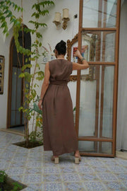Woman wearing a sleeveless brown crepe dress with a wide waist tie, standing indoors by an open door - sleeveless dress