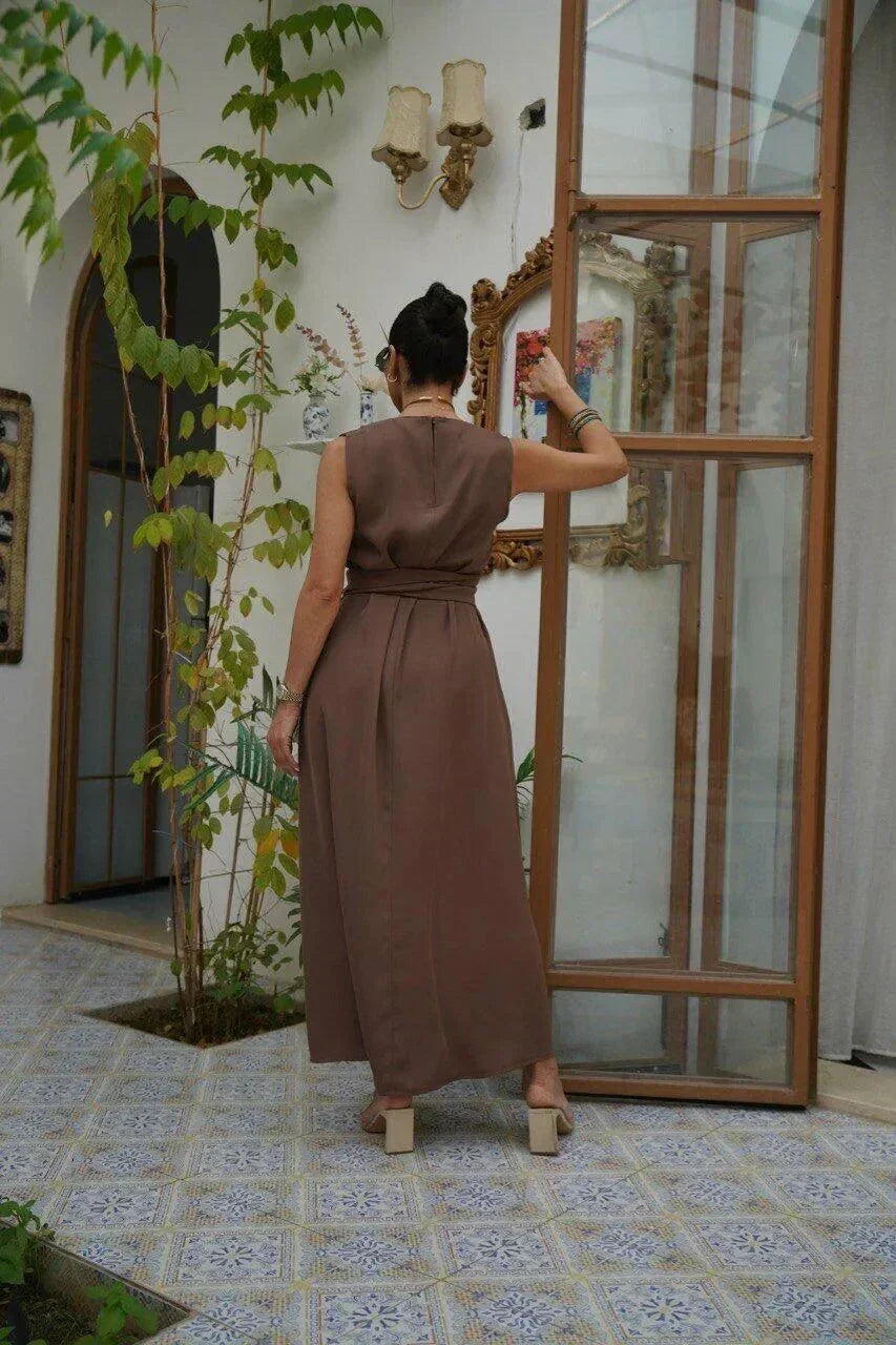 Woman wearing a sleeveless brown crepe dress with a wide waist tie, standing indoors by an open door - sleeveless dress