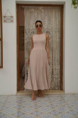 woman wearing sleeveless pleated beige dress with fitted top and flowing skirt