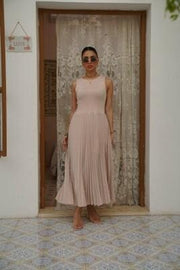woman wearing sleeveless pleated beige dress with fitted top and flowing skirt