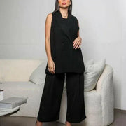 Woman wearing sleeveless black crepe double-breasted vest with sharp lapel collar styled with black wide-leg trousers in modern room - black crepe vest
