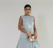 Woman wearing sleeveless sky blue linen vest with buttons, holding a small beige purse against a plain background